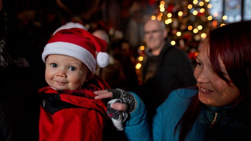 A small child in a Santa hat with their family and Christmas lights in the background